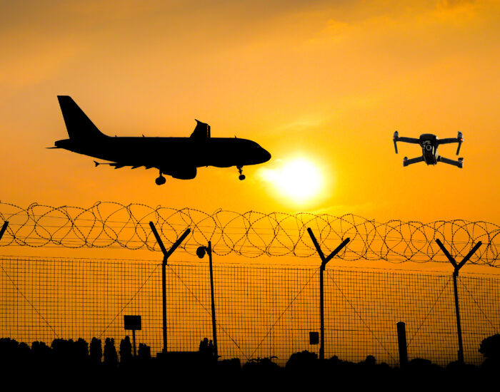 Unmanned drone flying over security fence at airport while commercial airplane prepares for landing, leading to possible collision