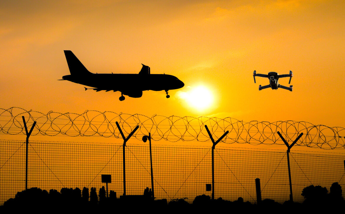 Unmanned drone flying over security fence at airport while commercial airplane prepares for landing, leading to possible collision